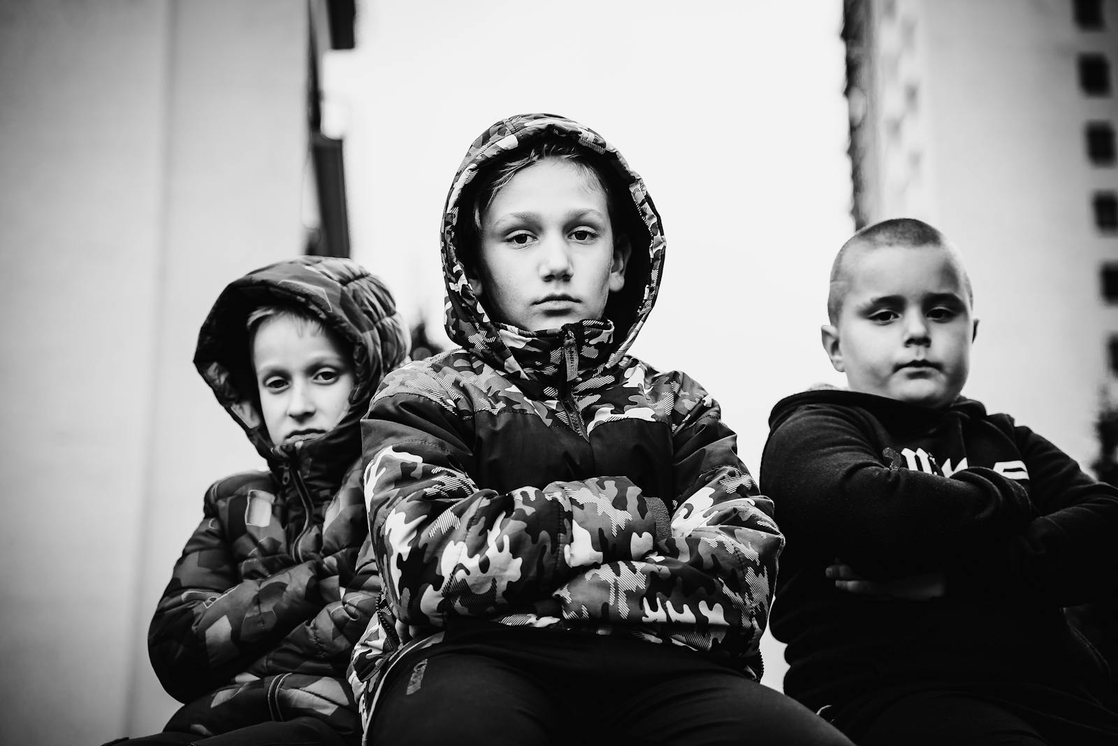 Grayscale image of three serious kids in hoodies, posing in an urban setting.