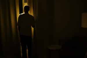 Silhouette of a person standing by a window in a dimly lit room, suggesting themes of solitude and contemplation.