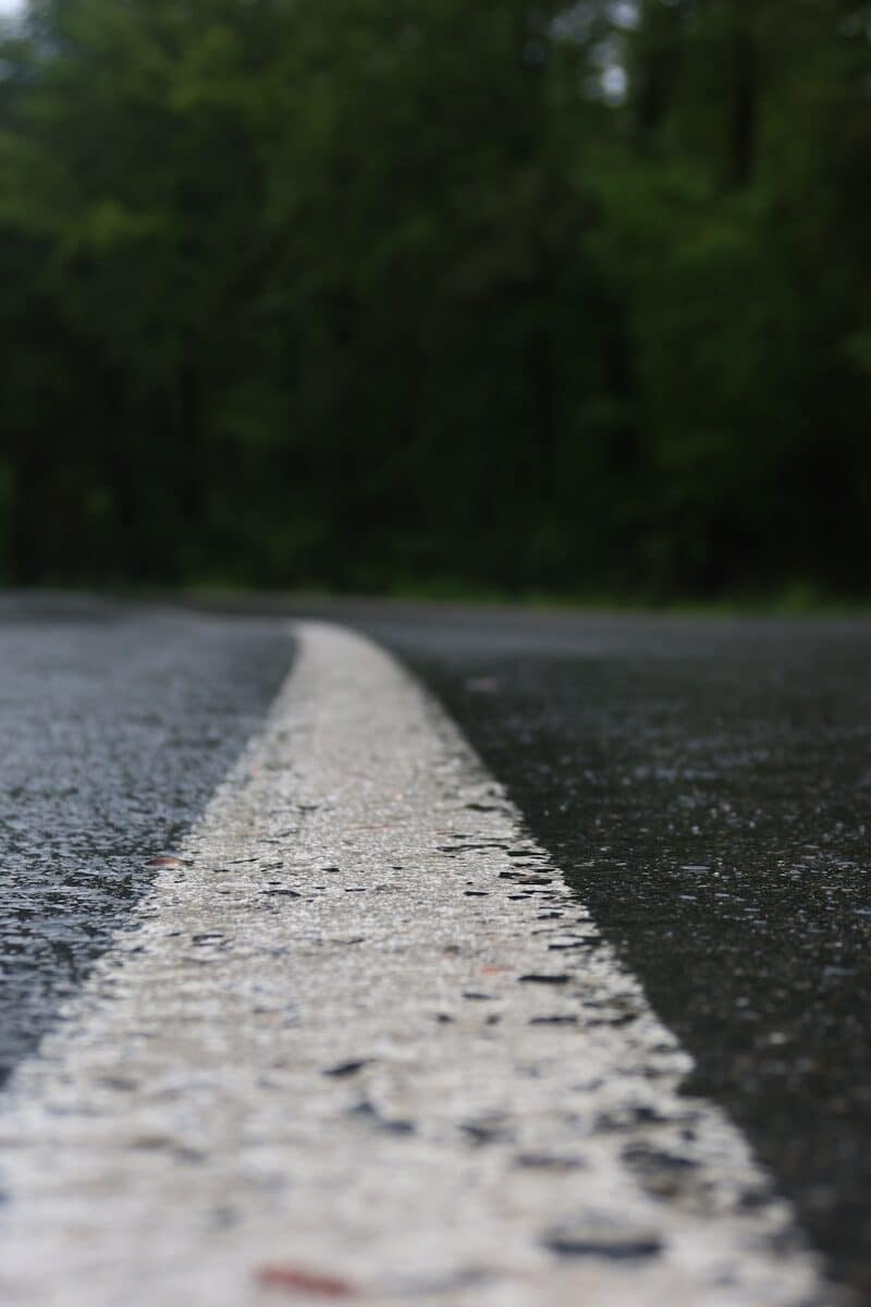 a white line on the side of a road with trees in the background