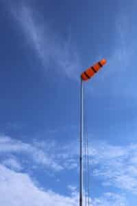 Orange and black windsock against a bright blue sky in Brighton, England.