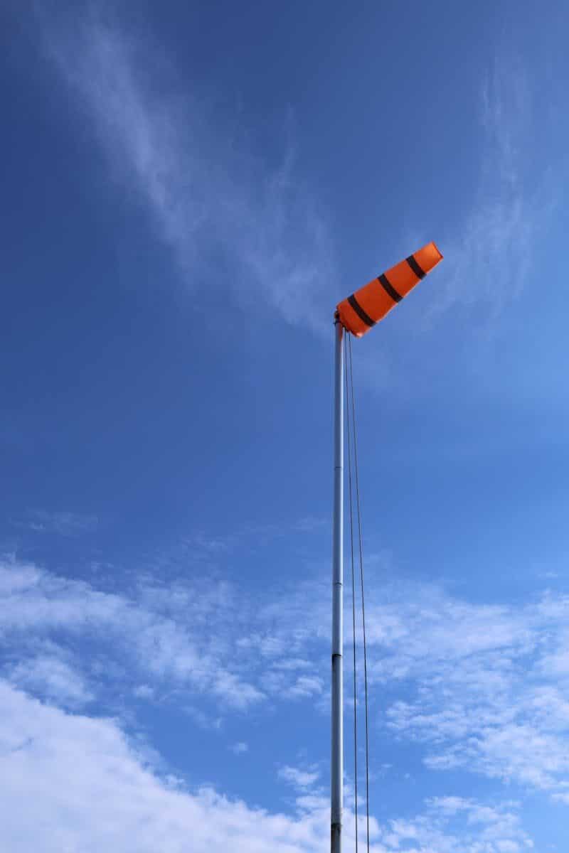 Orange and black windsock against a bright blue sky in Brighton, England.