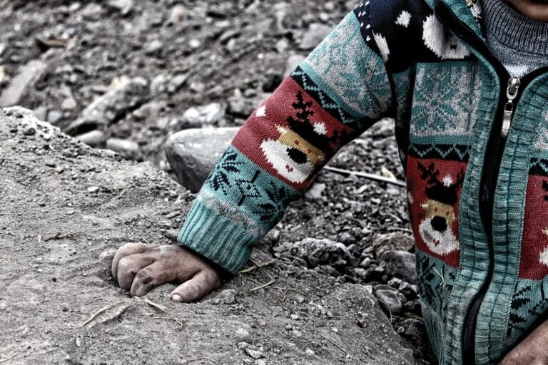 Close-up of a child's hand in a colorful sweater resting on soil, Erzurum, Türkiye.