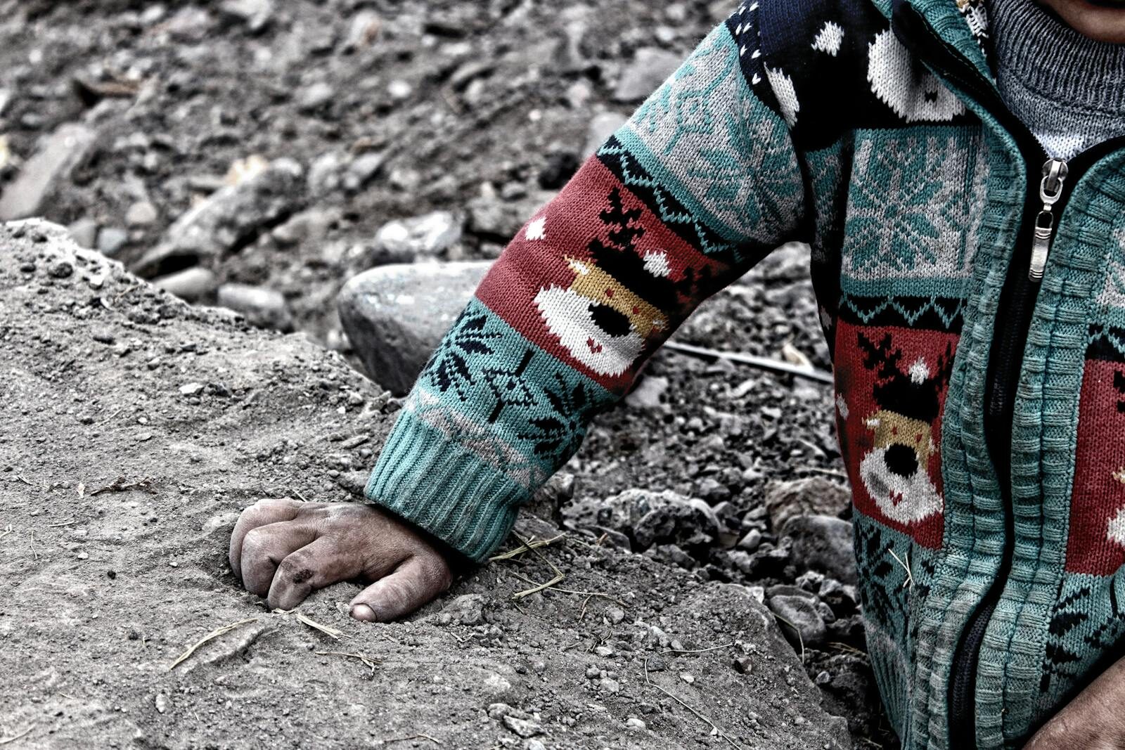 Close-up of a child's hand in a colorful sweater resting on soil, Erzurum, Türkiye.