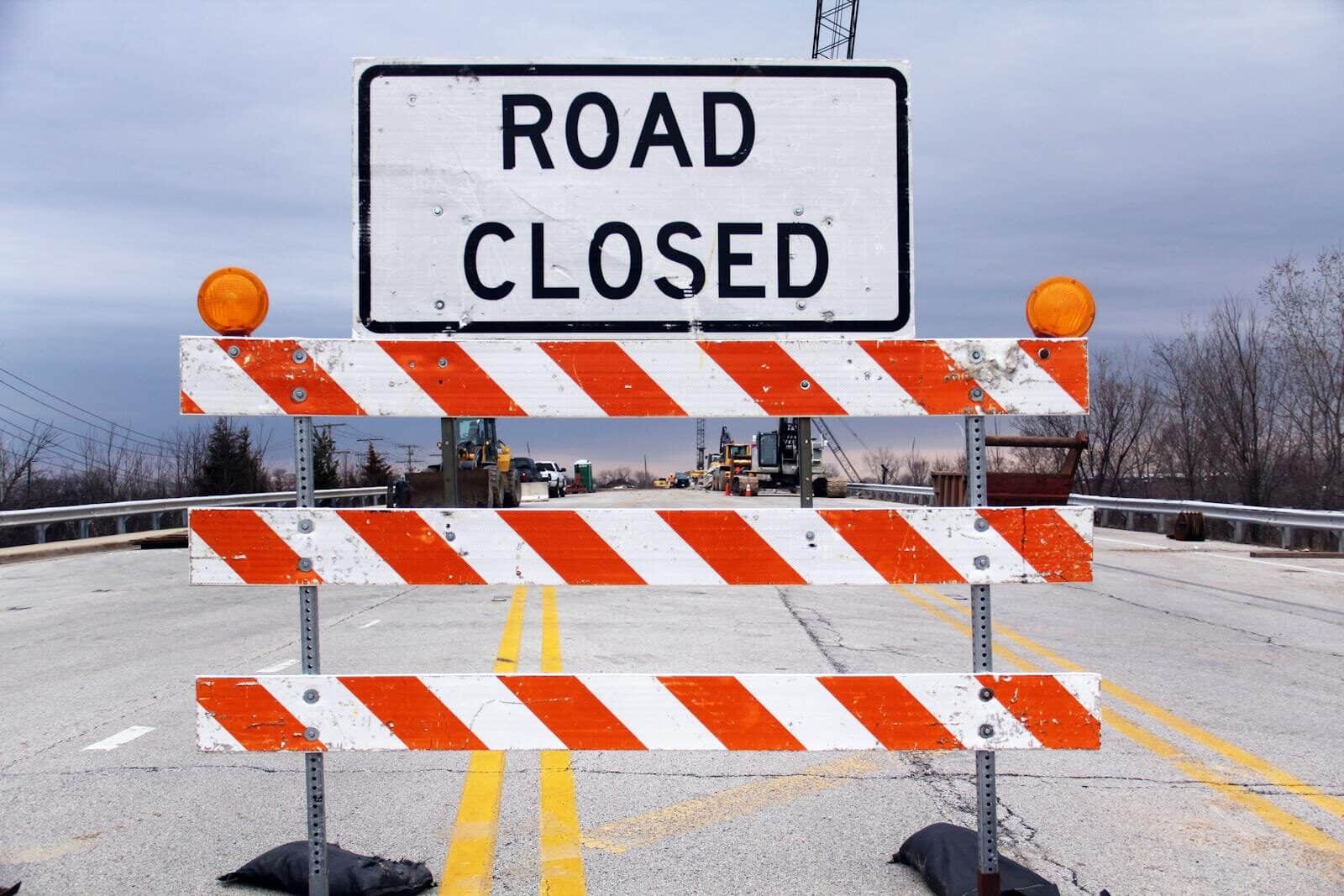 A road closed sign with barricade highlights caution on a suburban highway.