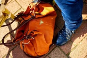 Orange leather bag paired with stylish footwear on sunny brick pavement.