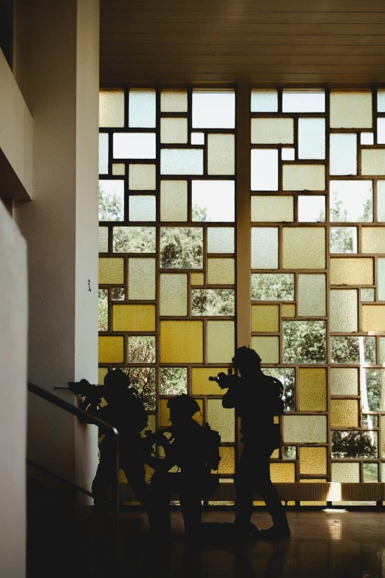 Silhouetted soldiers move cautiously near a patterned window.