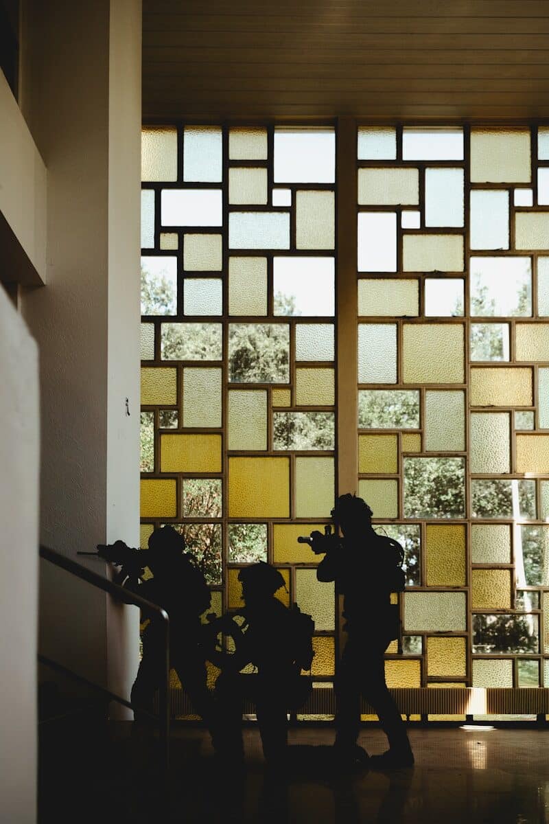 Silhouetted soldiers move cautiously near a patterned window.