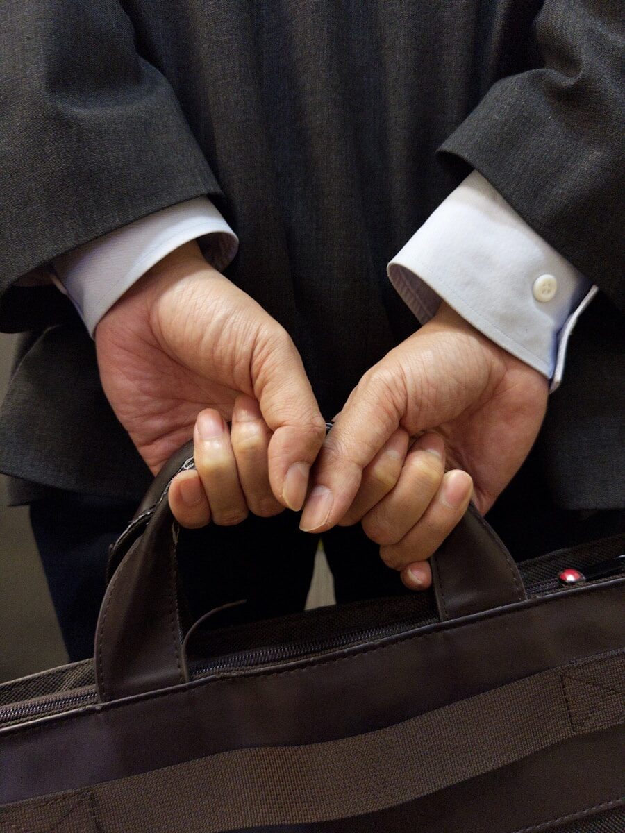 A businessman holds a briefcase behind his back.