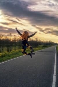 Girl joyfully jumps on a road beneath a sunset.