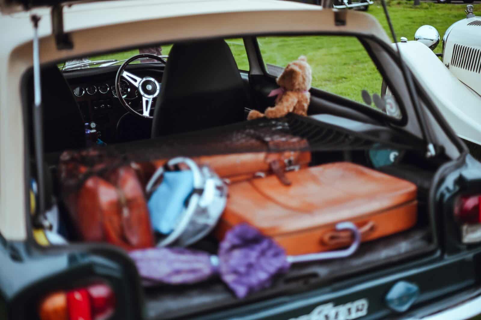 Open car trunk filled with luggage and teddy bear.
