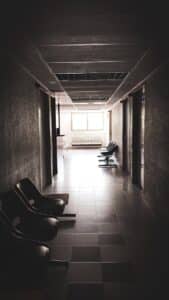 A dimly lit empty corridor with chairs and a waiting area, conveying a quiet atmosphere.
