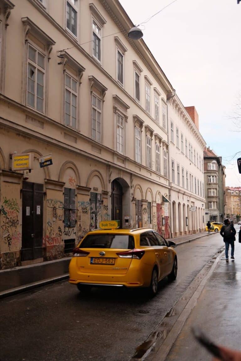 A vibrant urban street scene in Budapest featuring a yellow taxi and historic architecture, captured in daylight.