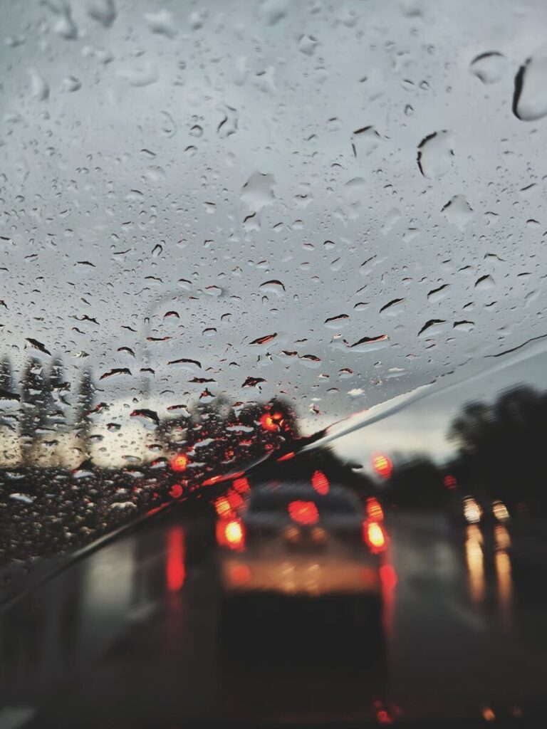 View of blurred traffic lights through a rain-covered windshield on a gloomy evening.
