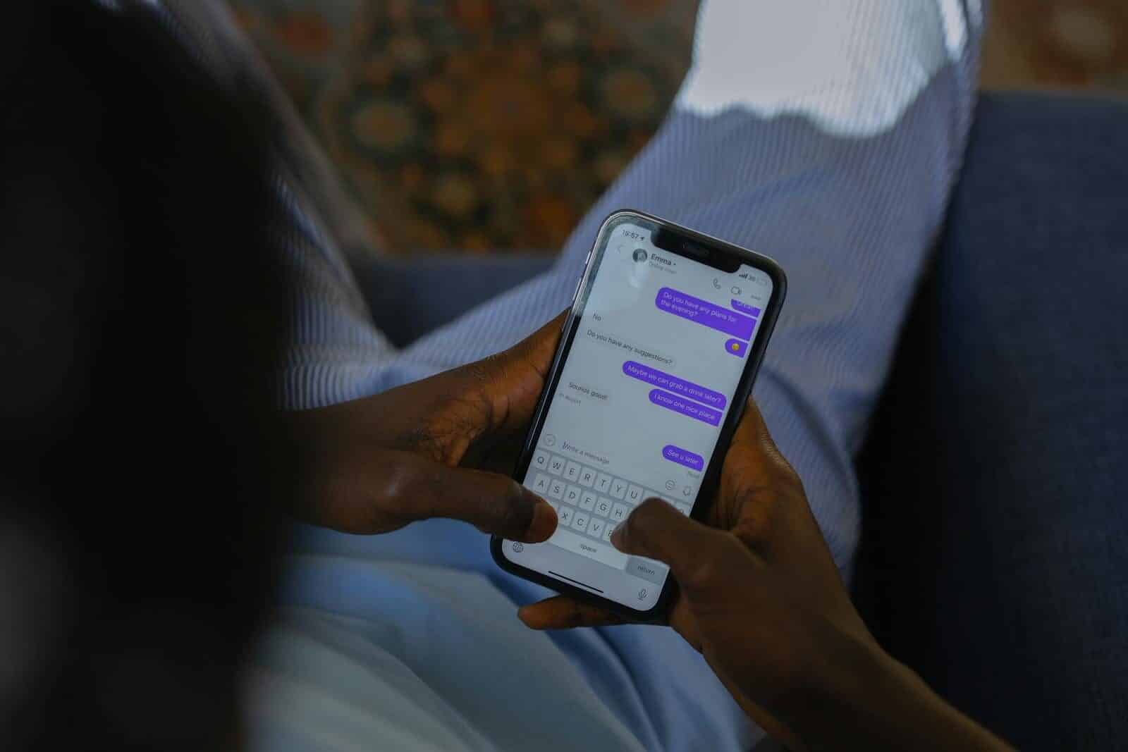 Close-up of hands holding a smartphone, typing a message on a touch screen indoors.