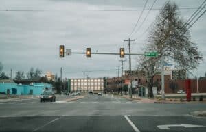 View of a city street intersection with traffic and buildings under a cloudy sky.