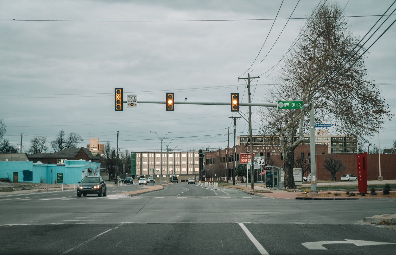 View of a city street intersection with traffic and buildings under a cloudy sky.