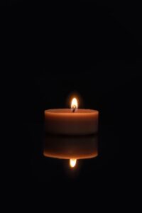 A single candle flame reflecting on a dark surface with a black background.