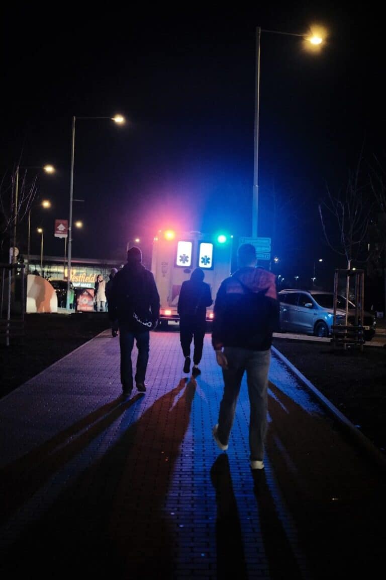 People walk towards an ambulance at night.