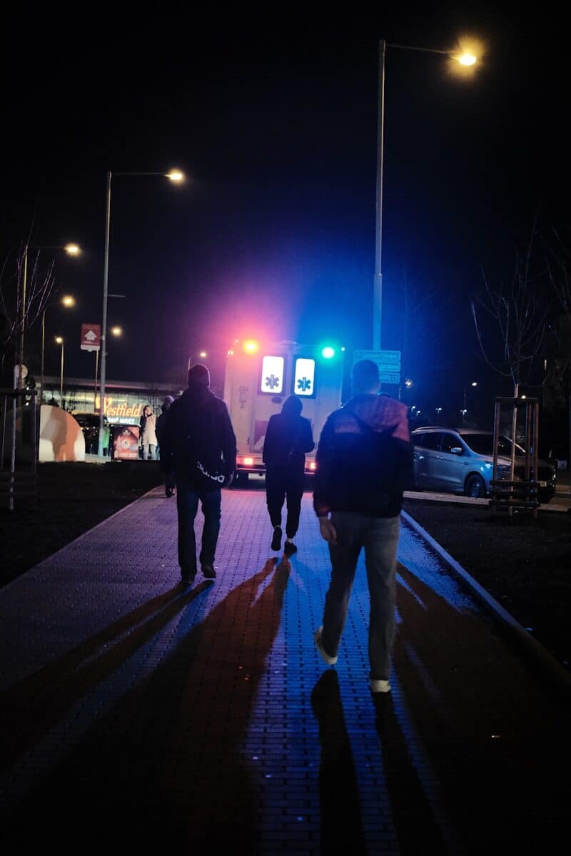 People walk towards an ambulance at night.