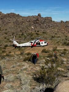 Helicopter lands in a rocky desert with rescue personnel