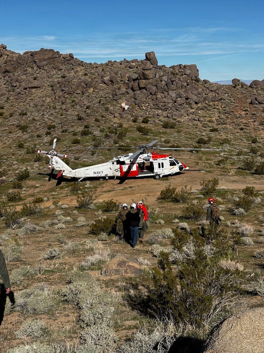 Helicopter lands in a rocky desert with rescue personnel
