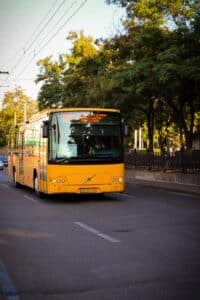 A yellow bus travels down a city street lined with trees during the day.