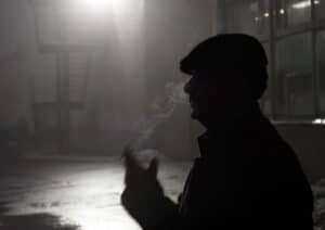A dramatic silhouette of a man smoking in an outdoor, nighttime setting.