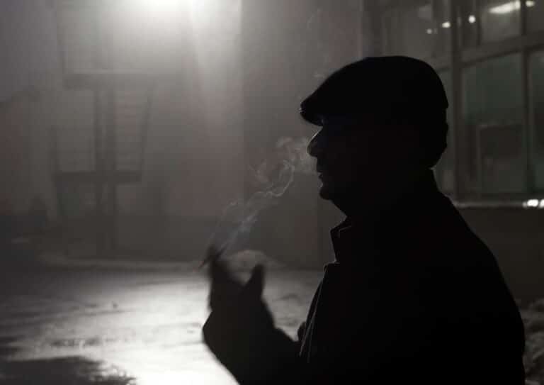 A dramatic silhouette of a man smoking in an outdoor, nighttime setting.