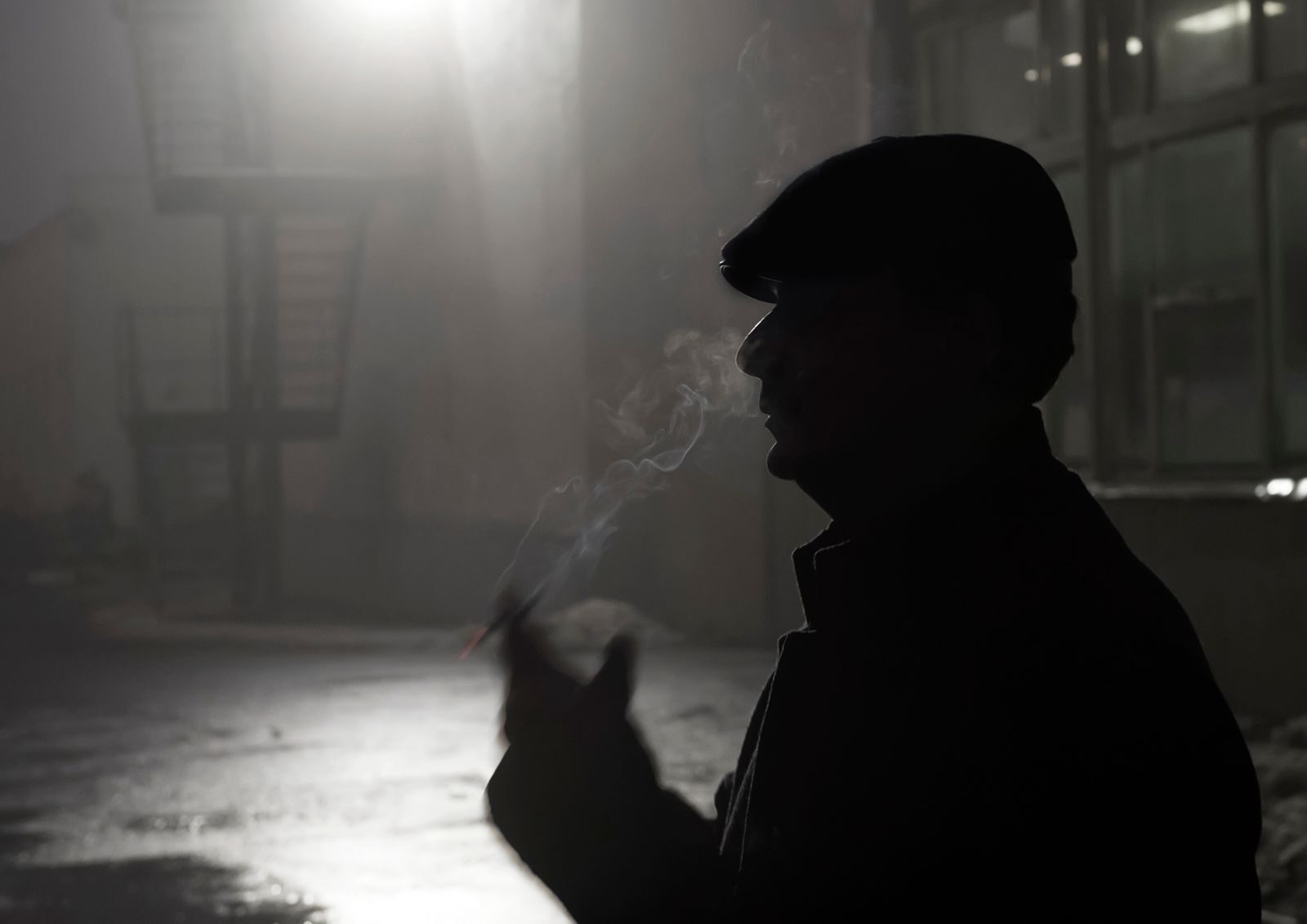 A dramatic silhouette of a man smoking in an outdoor, nighttime setting.
