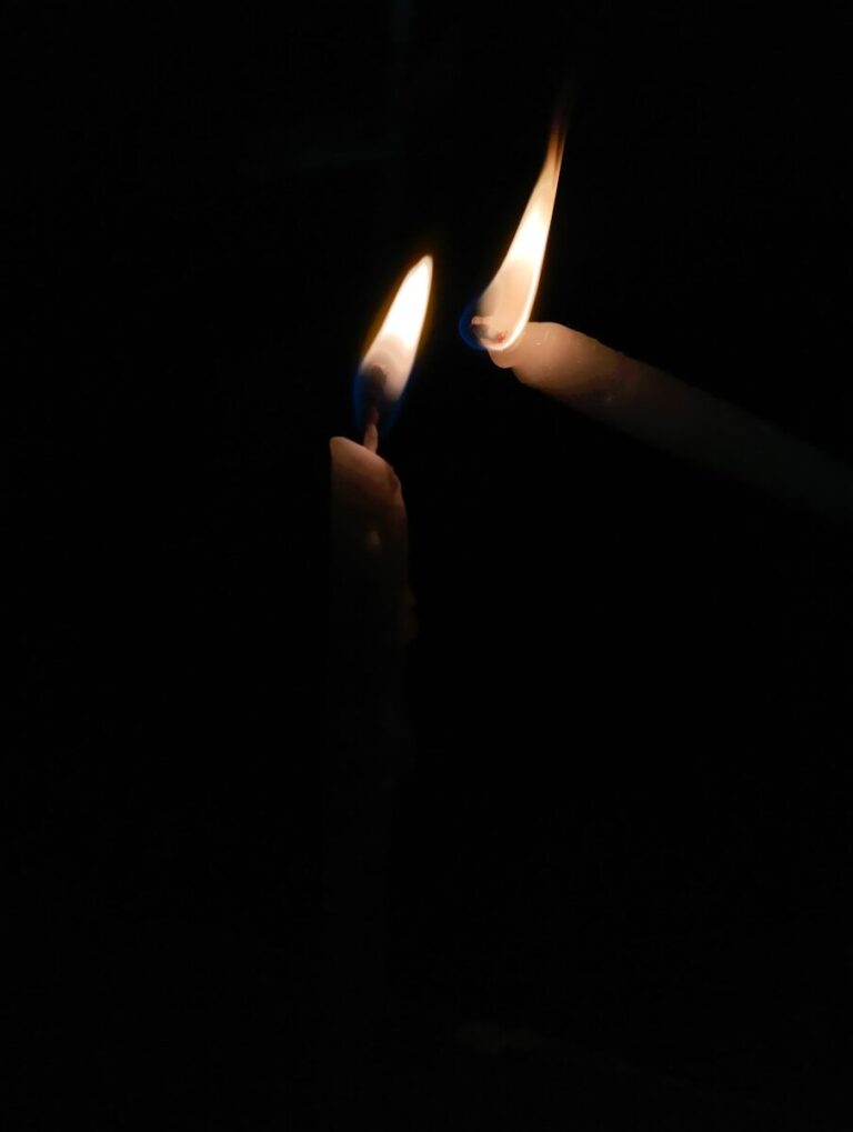 two lit candles in the dark with a black background