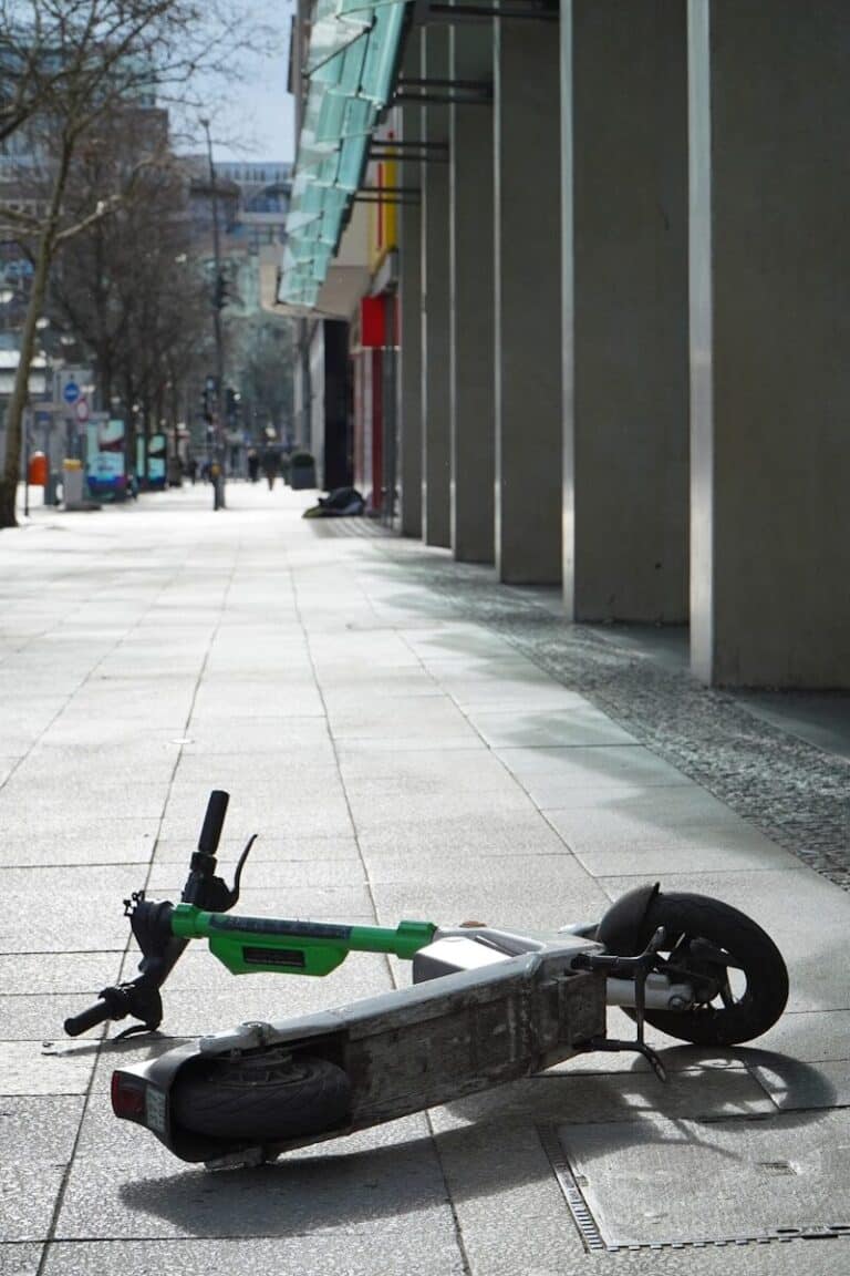 A lime scooter lies abandoned on a sidewalk.