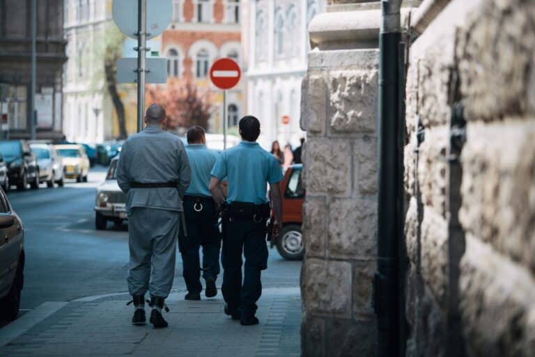 Policemen escort a handcuffed prisoner along a city street, showcasing law enforcement in action.
