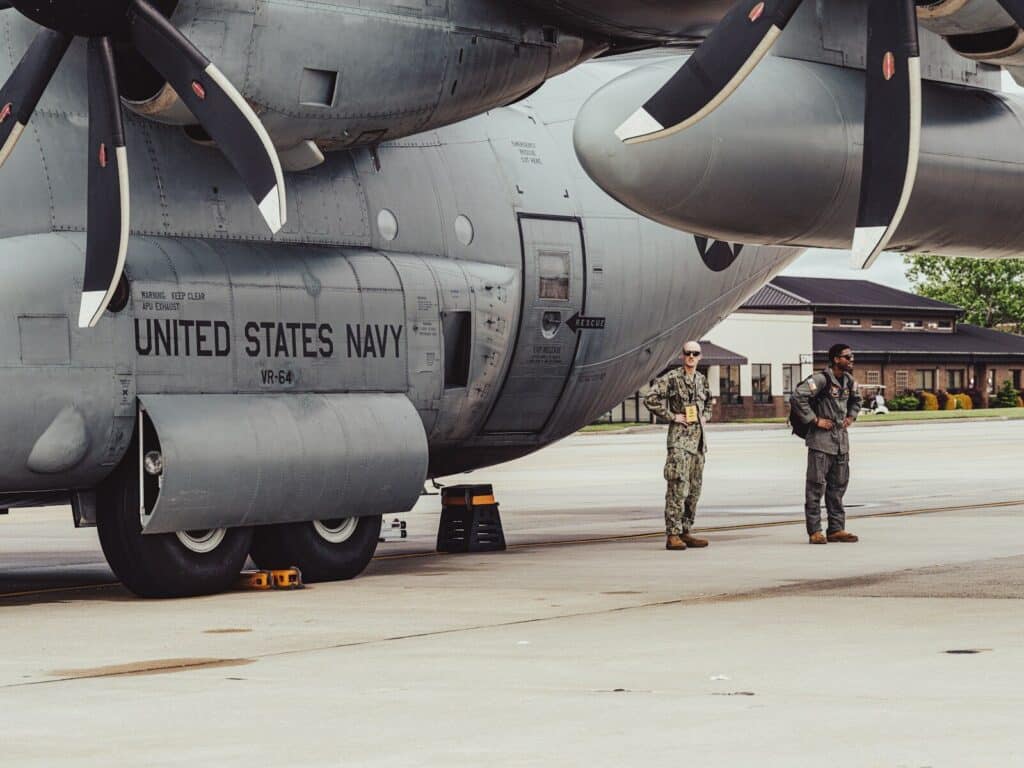 Two navy personnel stand by a military aircraft