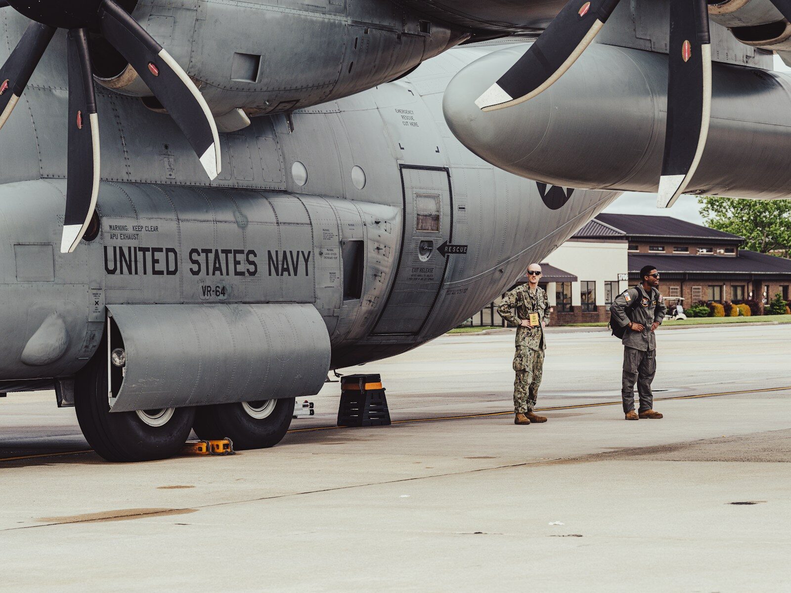 Two navy personnel stand by a military aircraft