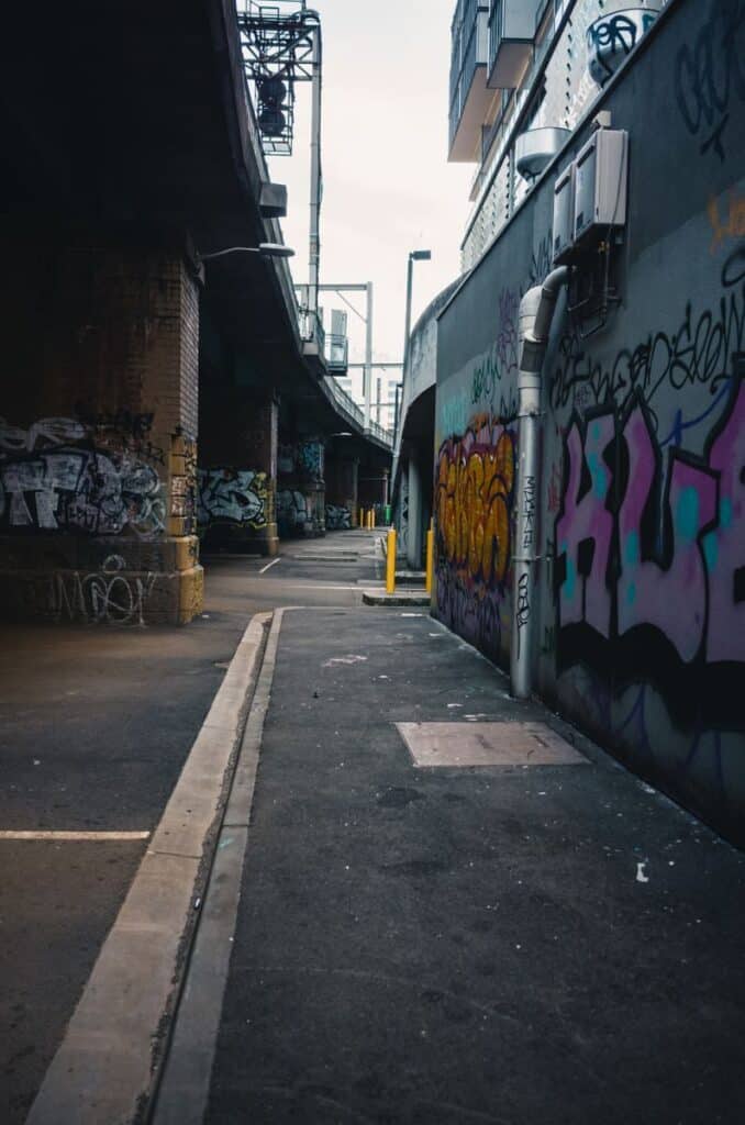 Vibrant graffiti decorates the walls of a deserted urban alley beneath an overpass.