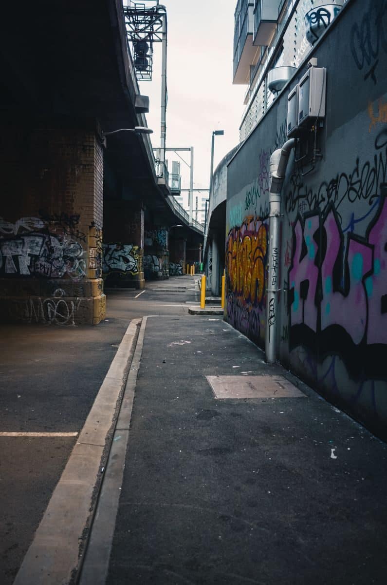 Vibrant graffiti decorates the walls of a deserted urban alley beneath an overpass.