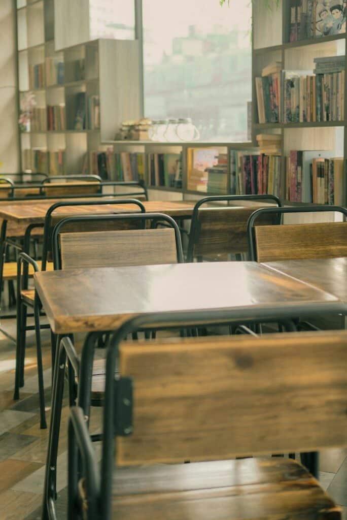 Empty wooden tables and chairs in a library with shelves of books