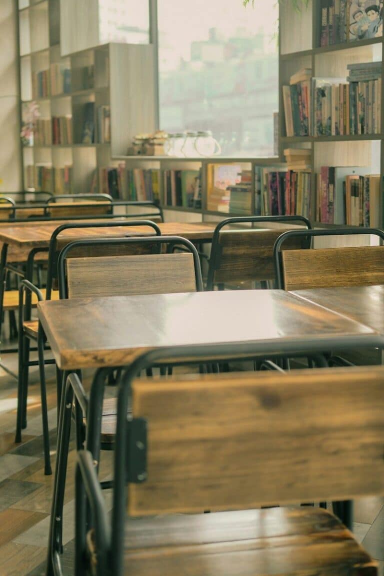Empty wooden tables and chairs in a library with shelves of books