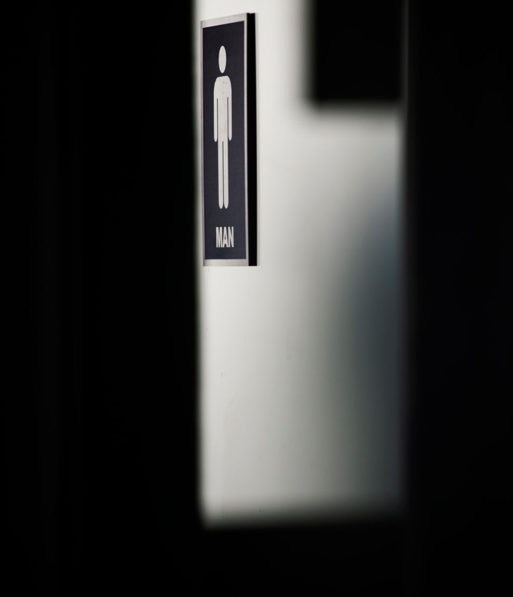 Moody close-up photo of a men's restroom sign with a focus on shadows and minimalistic design.